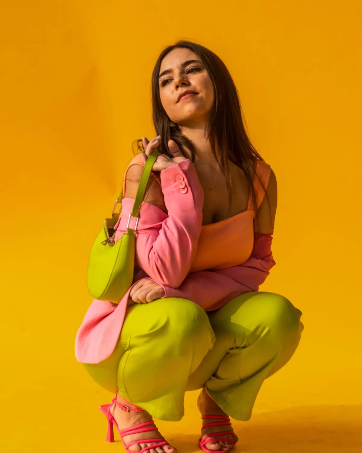 Modelo de blazer rosa e calça verde-limão sobre fundo amarelo