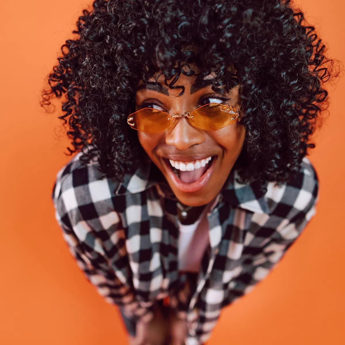 Mulher sorrindo de camisa xadrez sobre fundo laranja